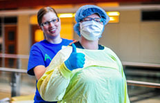 A medical student helps a camper with trying on surgery gear